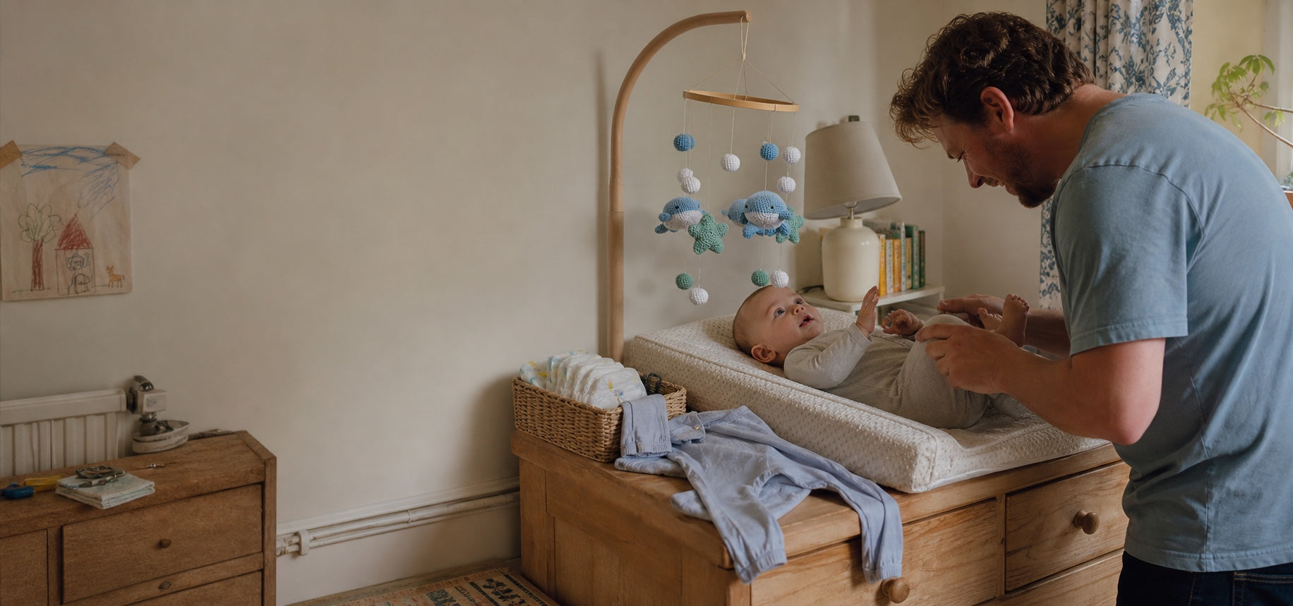 Parent changing a baby beneath an Aven and Oak whale mobile