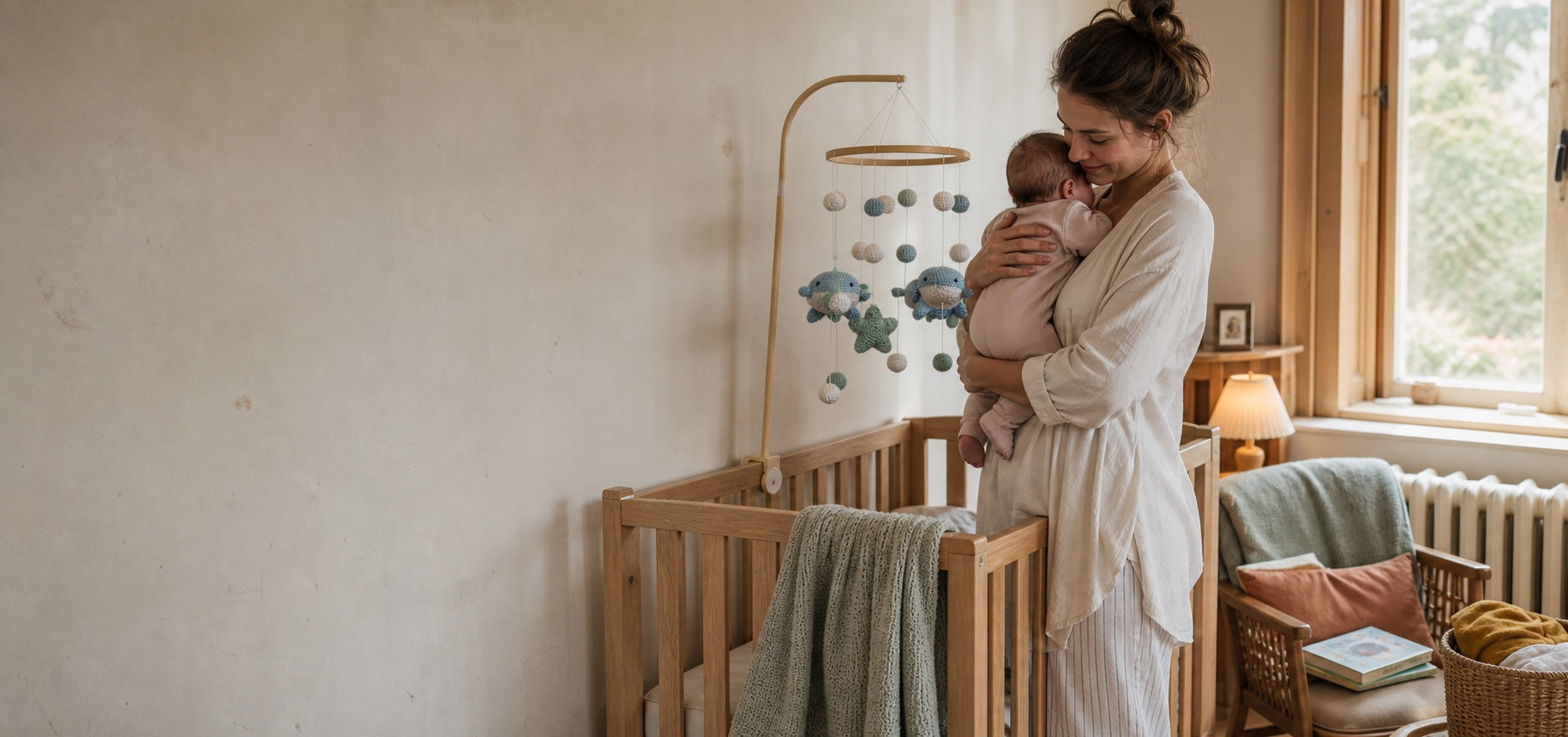 Parent holding a newborn beside an Aven and Oak whale mobile in a warm nursery