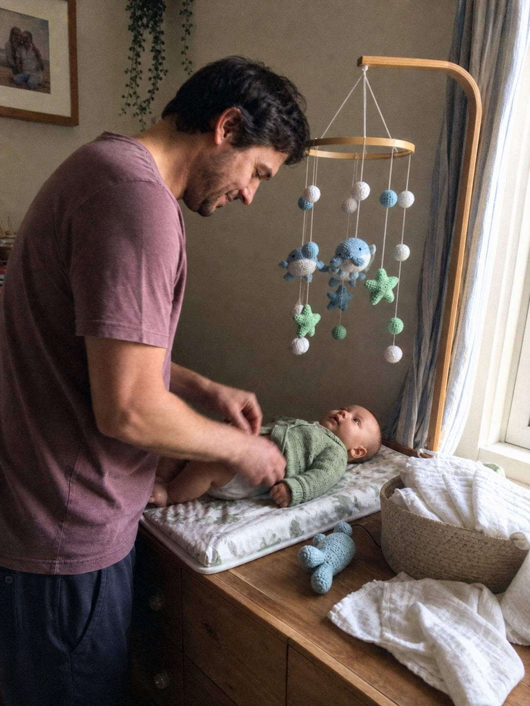 Father changing his baby beneath an Aven and Oak whale mobile